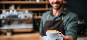 Ein Barista hält eine Kaffeetasse in Richtung des Bildbetrachters