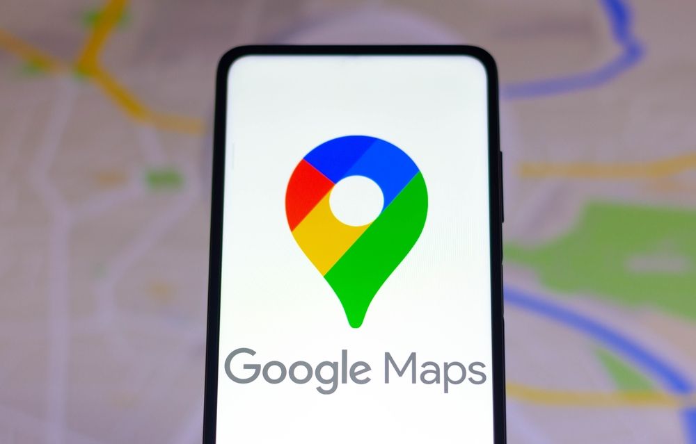 Nahaufnahme eines Smartphones, auf dem das Google-Maps-Logo zu sehen ist, mit einer Karte, wie man sie in Google Maps sehen würde, im Hintergrund.