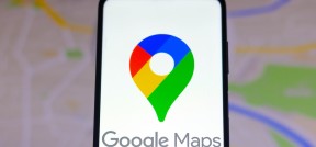 Nahaufnahme eines Smartphones, auf dem das Google-Maps-Logo zu sehen ist, mit einer Karte, wie man sie in Google Maps sehen würde, im Hintergrund.