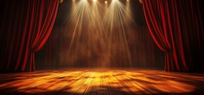Das Bild zeigt eine leere Bühne wie im Theater mit roten Vorhängen an den Seiten und Scheinwerfern oben.