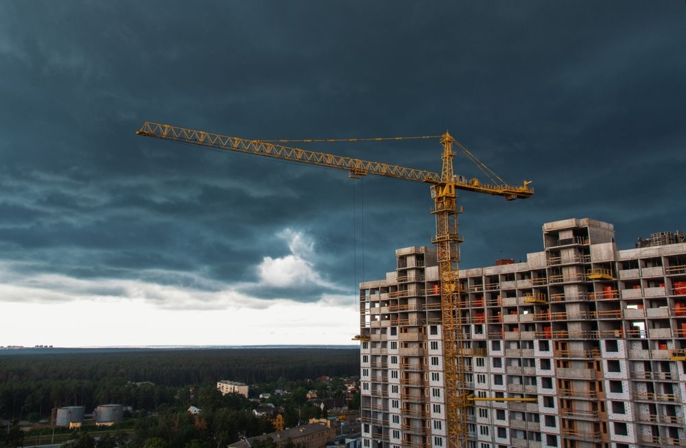 Das Bild zeigt einen Baukrahn vor einem unfertigem Hochhaus zum Wohnen.