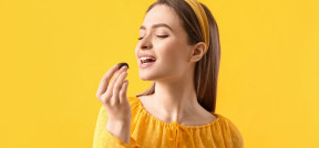 Auf dem Bild sieht man eine Frau vor gelbem Hintergrund, die kurz davor ist, in eine Praline zu beißen. Sie trägt gelbe Kleidung.
