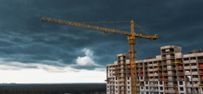 Das Bild zeigt einen Baukrahn vor einem unfertigem Hochhaus zum Wohnen.