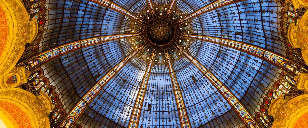 Blick von unten in die bläulich-golden schimmernde Glaskuppel der Galeries Lafayette in Paris
